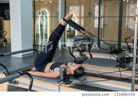 Caucasian woman doing exercises on reformer machine. Caucasian woman doing exercises on reformer machine. 135906350