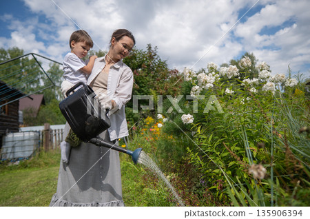 Caucasian woman and her son watering flowers in the garden.  135906394