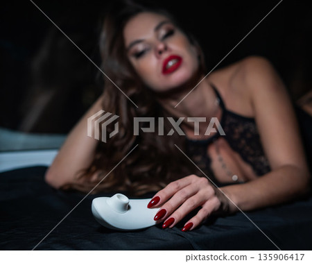 Woman in lace lingerie holding white clitoral vacuum stimulator.  135906417