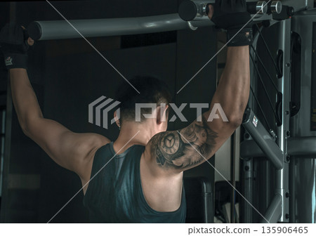 The back of bodybuilders exercise with lifting weights on an exercising machine in gym or fitness club. The back of bodybuilders exercise with lifting weights on an exercising machine in gym or fitness club. 135906465