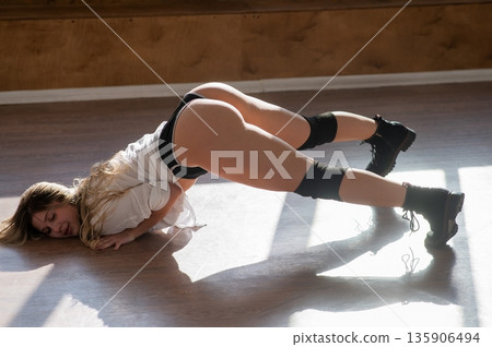 A young woman dances twerk in short shorts on the floor. A young woman dances twerk in short shorts on the floor. 135906494