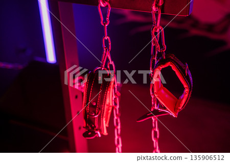 A close-up of BDSM equipment. Leather handcuffs on chains. 135906512