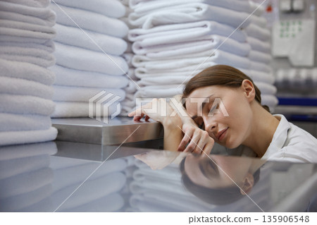 A woman is peacefully sleeping in front of a large stack of towels 135906548
