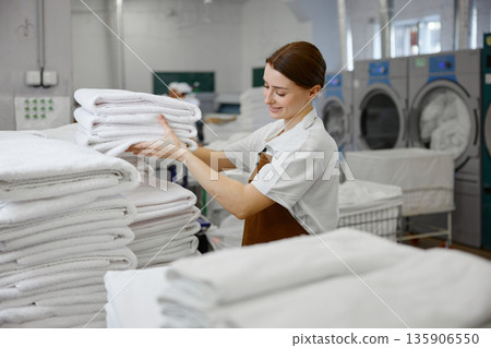 A woman worker is stacking towels neatly on a table in a laundromat 135906550