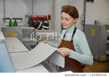 Young woman worker is ironing towels on a table in a laundromat Young woman worker is ironing towels on a table in a laundromat 135906556