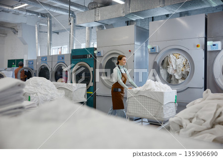 A woman worker is pushing a cart filled with clothes in a laundromat 135906690