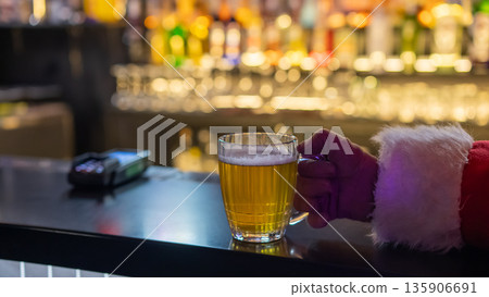Santa Claus drinking beer at a bar. Close-up of a hand holding a mug of beer.  135906691