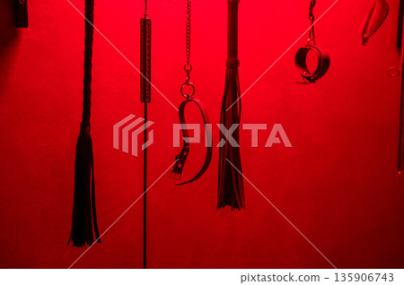 Collection of BDSM toys, whips in red light. Collection of BDSM toys, whips in red light. 135906743