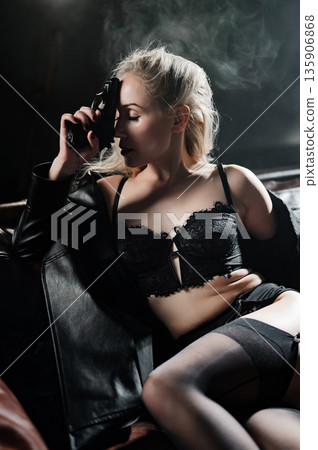 A Caucasian woman poses with a gun on a leather sofa.  135906868