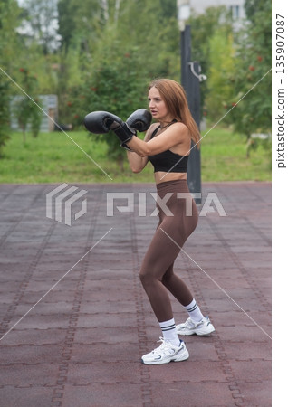 A Caucasian woman practices boxing outdoors.  135907087