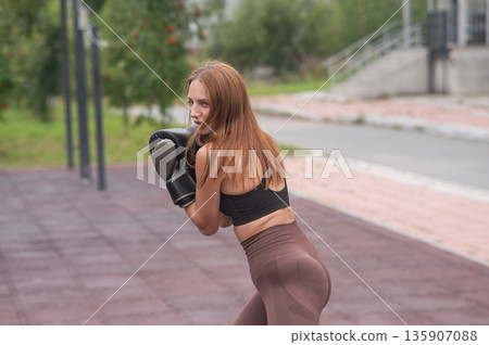 A Caucasian woman practices boxing outdoors.  135907088