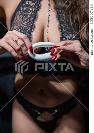 A woman in black lingerie holds a curved vibrator.  135907159