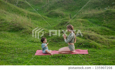 Caucasian woman doing yoga with her little son outdoors.  135907208