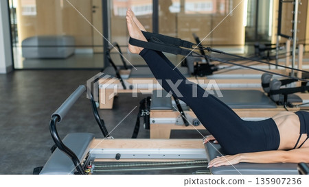 Caucasian woman doing exercises on reformer machine. Caucasian woman doing exercises on reformer machine. 135907236