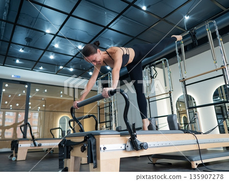 Caucasian woman doing exercises on reformer machine. Caucasian woman doing exercises on reformer machine. 135907278
