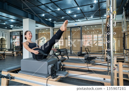Caucasian woman doing exercises on reformer machine. Caucasian woman doing exercises on reformer machine. 135907281