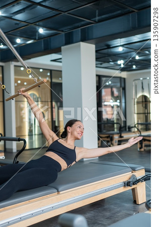 Caucasian woman doing exercises on reformer machine. Caucasian woman doing exercises on reformer machine. 135907298