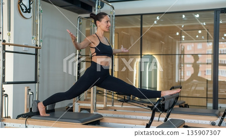 Caucasian woman doing splits on reformer. Caucasian woman doing splits on reformer. 135907307