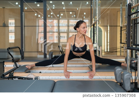 Caucasian woman doing side splits on reformer. Caucasian woman doing side splits on reformer. 135907308