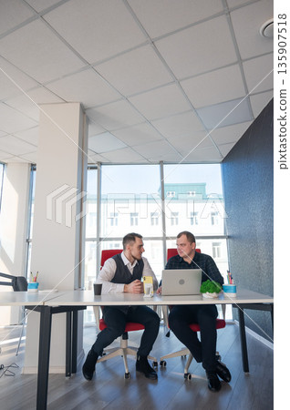 Two Caucasian men sitting at a table and discussing work.  135907518