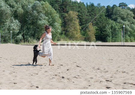 Caucasian woman walking on the beach with her dog.  135907569