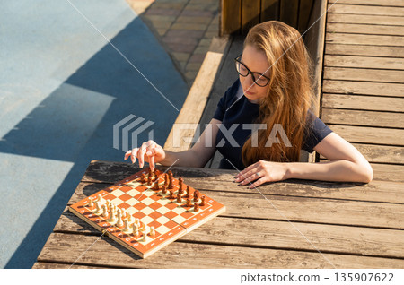 Caucasian woman playing chess outdoors. 135907622