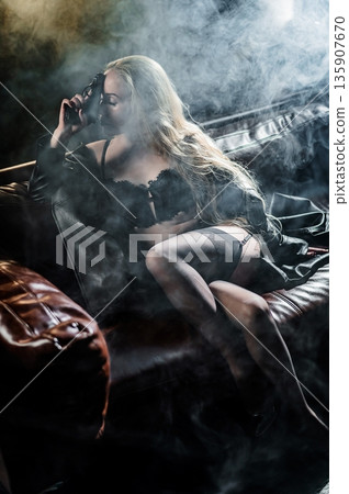A Caucasian woman poses with a gun on a leather sofa. A Caucasian woman poses with a gun on a leather sofa. 135907670