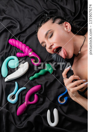 Portrait of Caucasian woman lying on bed among sex toys.  135907674