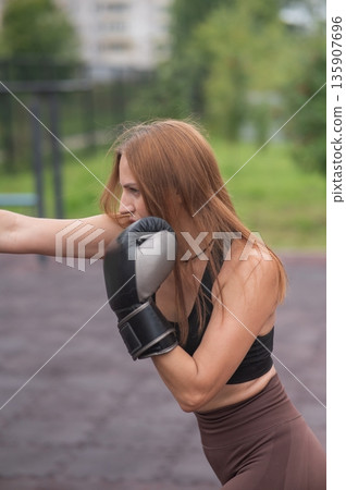 A Caucasian woman practices boxing outdoors.  135907696