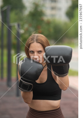 A Caucasian woman practices boxing outdoors.  135907697