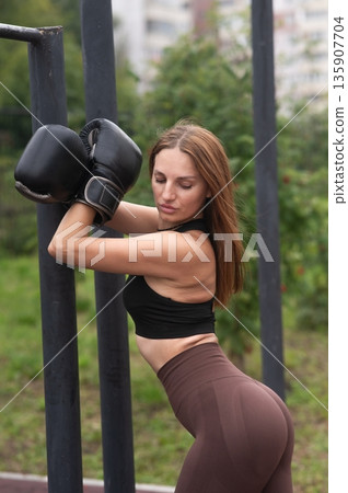 A Caucasian woman poses in boxing gloves on a sports field. 135907704