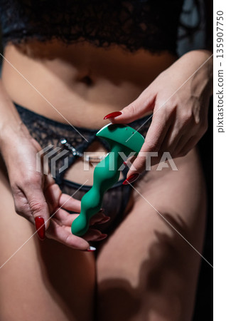 Woman in lace lingerie holding green anal beads.  135907750