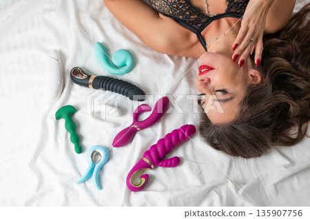 A beautiful Caucasian woman in black lingerie lies among sex toys.  135907756