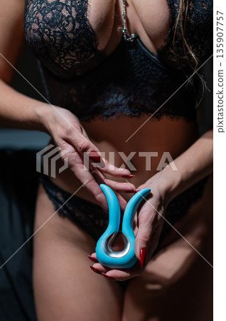 A woman in black lingerie holds a curved vibrator.  135907757