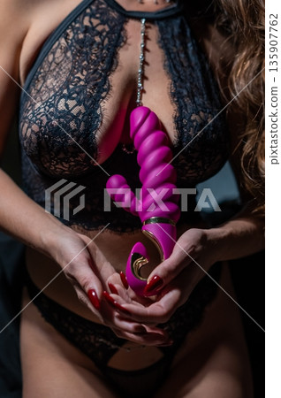 Woman in lace lingerie holds pink dildo.  135907762