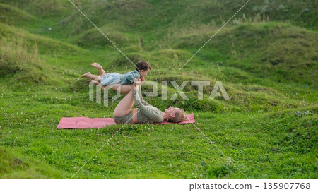 Caucasian woman doing yoga with her little son outdoors.  135907768