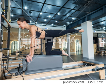 Caucasian woman doing leg exercise on reformer machine. Caucasian woman doing leg exercise on reformer machine. 135907794