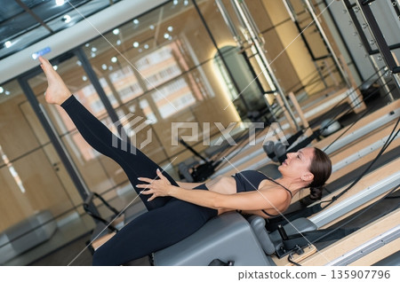 Caucasian woman doing exercises on reformer machine. Caucasian woman doing exercises on reformer machine. 135907796