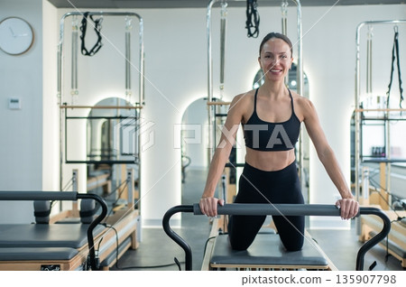 Caucasian woman doing exercises on reformer machine. Caucasian woman doing exercises on reformer machine. 135907798