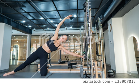 Caucasian woman doing side bends on reformer machine. Caucasian woman doing side bends on reformer machine. 135907815
