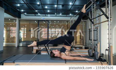Caucasian woman doing leg exercise on reformer machine.  135907826