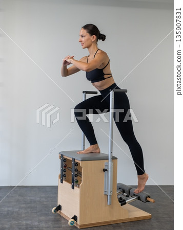 Caucasian woman doing Pilates on classic chair. 135907831
