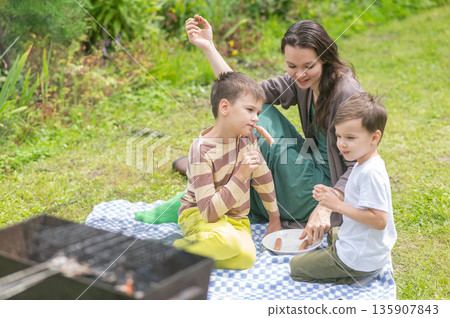 Caucasian woman eats fried sausages with her sons at a picnic.  135907843