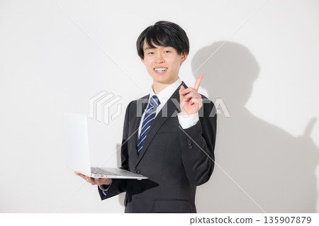 A young man in a suit, resembling a university student, holding a laptop on a white background. Image of a new graduate or job-hunting employee. 135907879