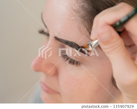 Caucasian woman getting eyebrow tinting procedure. Caucasian woman getting eyebrow tinting procedure. 135907929