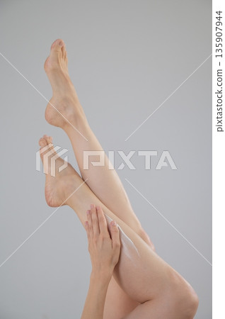 Woman applying moisturizer to her legs. White background.  135907944