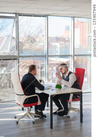 Two Caucasian men communicating at a business meeting. Two Caucasian men communicating at a business meeting. 135907949