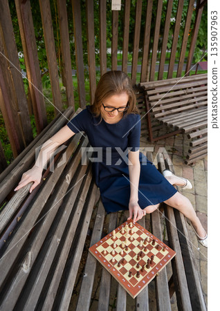 Caucasian woman playing chess outdoors. 135907963