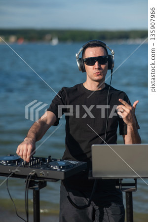 Male DJ playing music on the beach. Male DJ playing music on the beach. 135907966