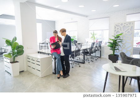 Colleagues look at a folder with documents and discuss work issues.  135907971